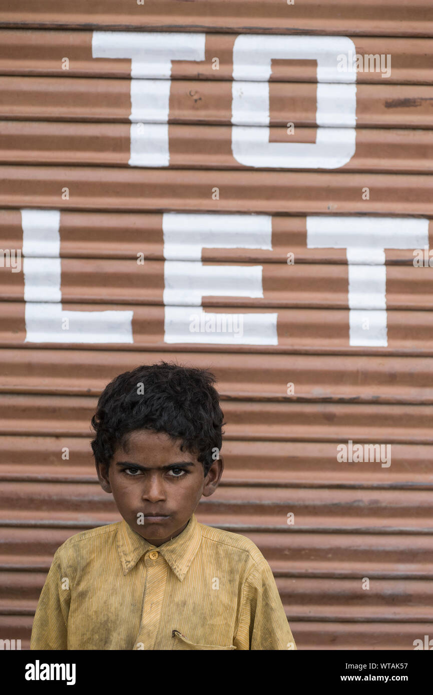 Homeless kid in front of a shop`s steel door Stock Photo